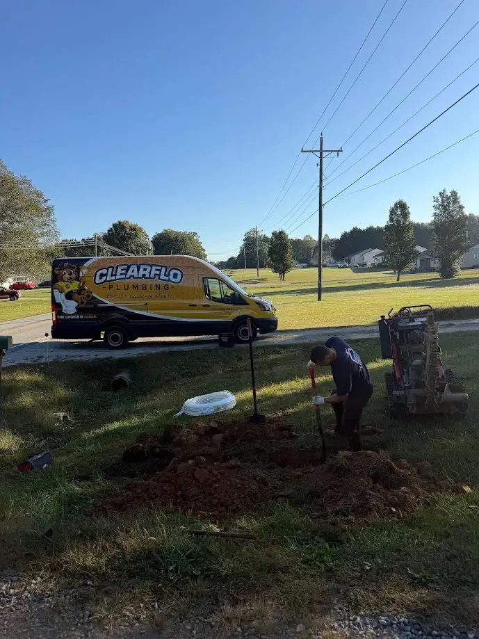 Two construction workers in safety vests connect pipes in a trench during roadwork.