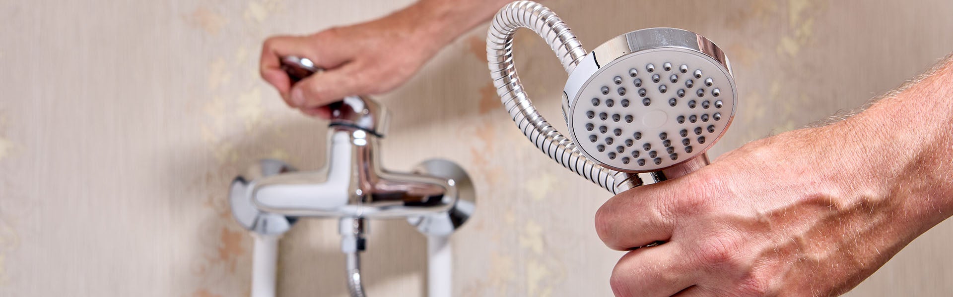 Hands adjust a chrome shower head and faucet with a flexible hose.