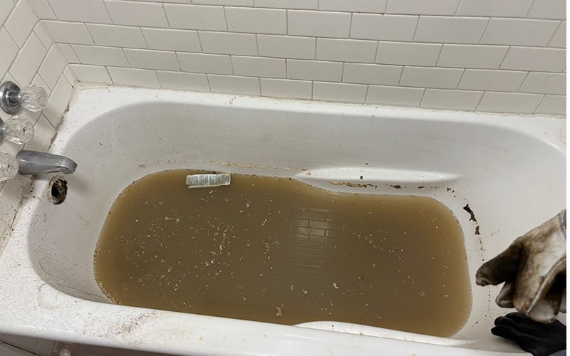 A dirty white bathtub contains murky brown water and debris near the drain.