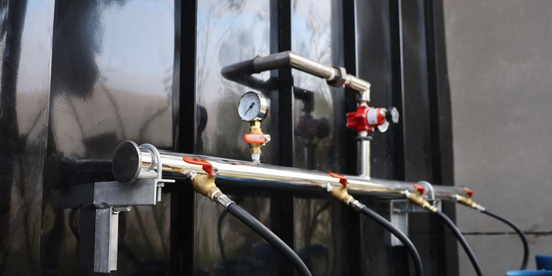 Industrial machinery features pipes, valves, and a gauge against a black background.