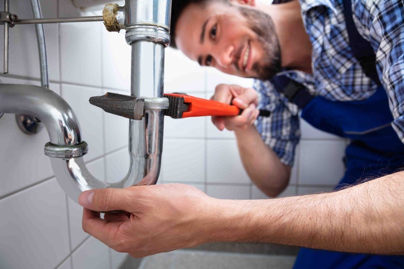 A plumber uses pliers to tighten a pipe fitting beneath a bathroom sink.
