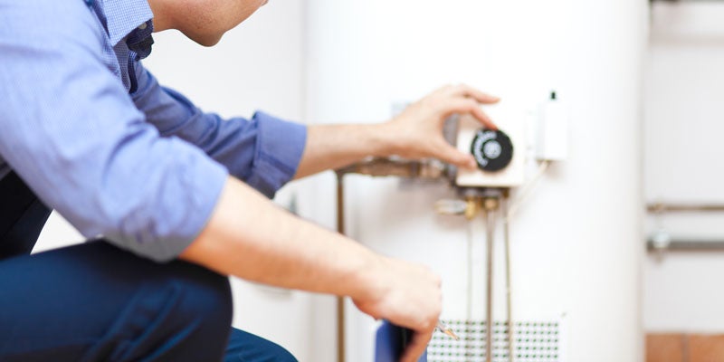A person in a blue shirt adjusts a valve on a white water heater.